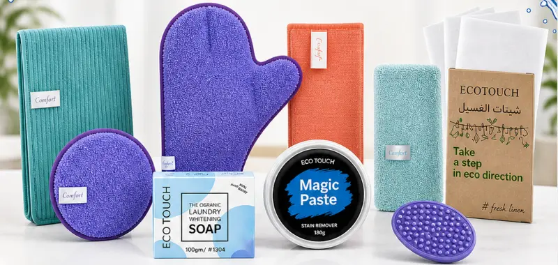 مجموعة من منتجات التنظيف EcoTouch على سطح أبيض. تحتوي على أقمشة و"معجون سحري" و"صابون تبييض الغسيل العضوي" وصندوق يحمل عبارة "اتخذ خطوة في الاتجاه البيئي".